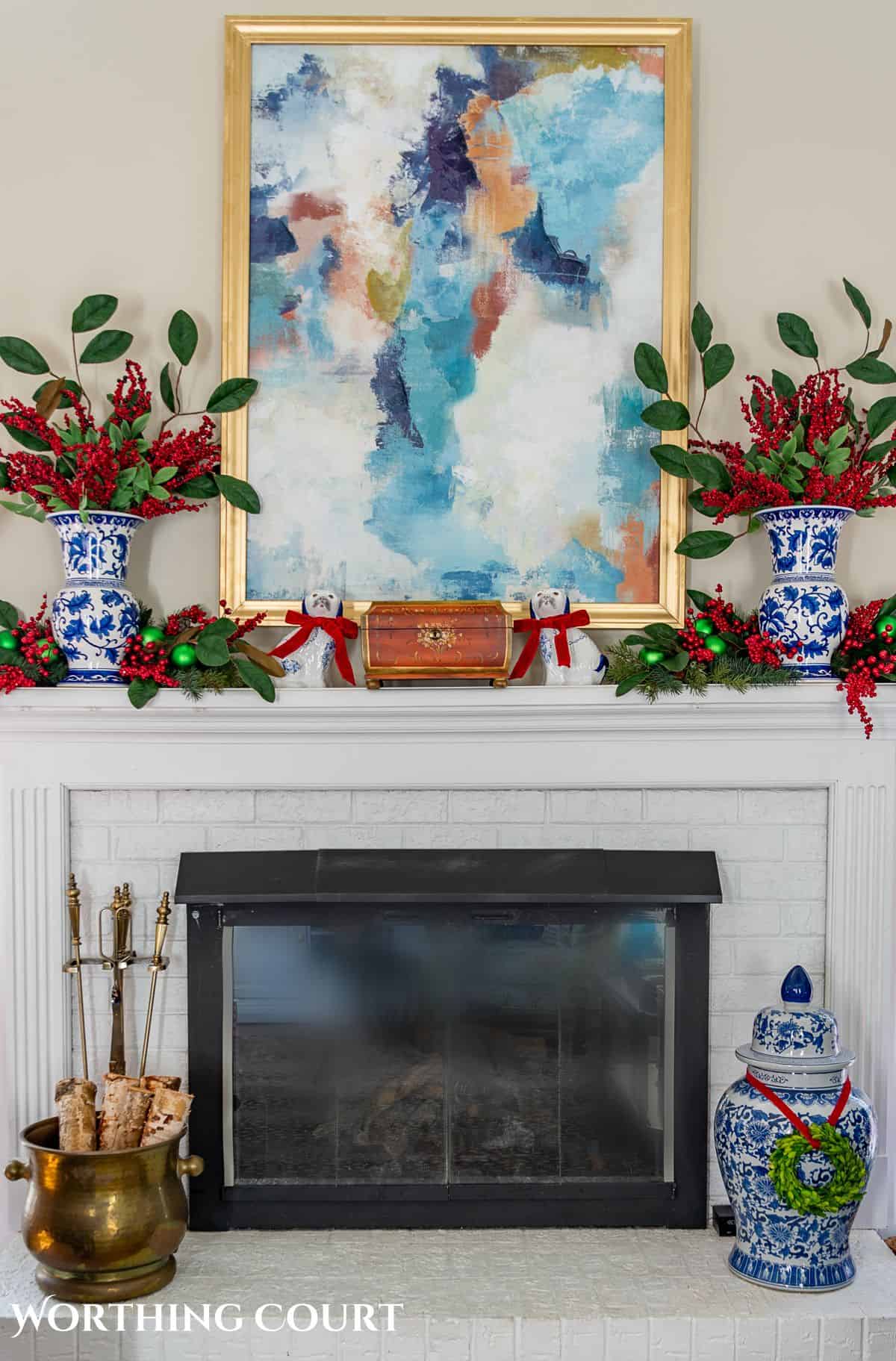 fireplace mantel with abstract art above and traditional Christmas decorations mixed with chinoiserie decor items