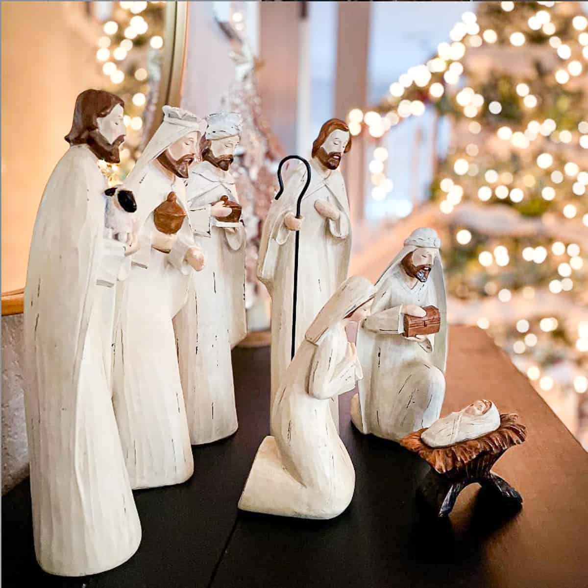 white nativity set on a brown chest with a lite Christmas tree in the background