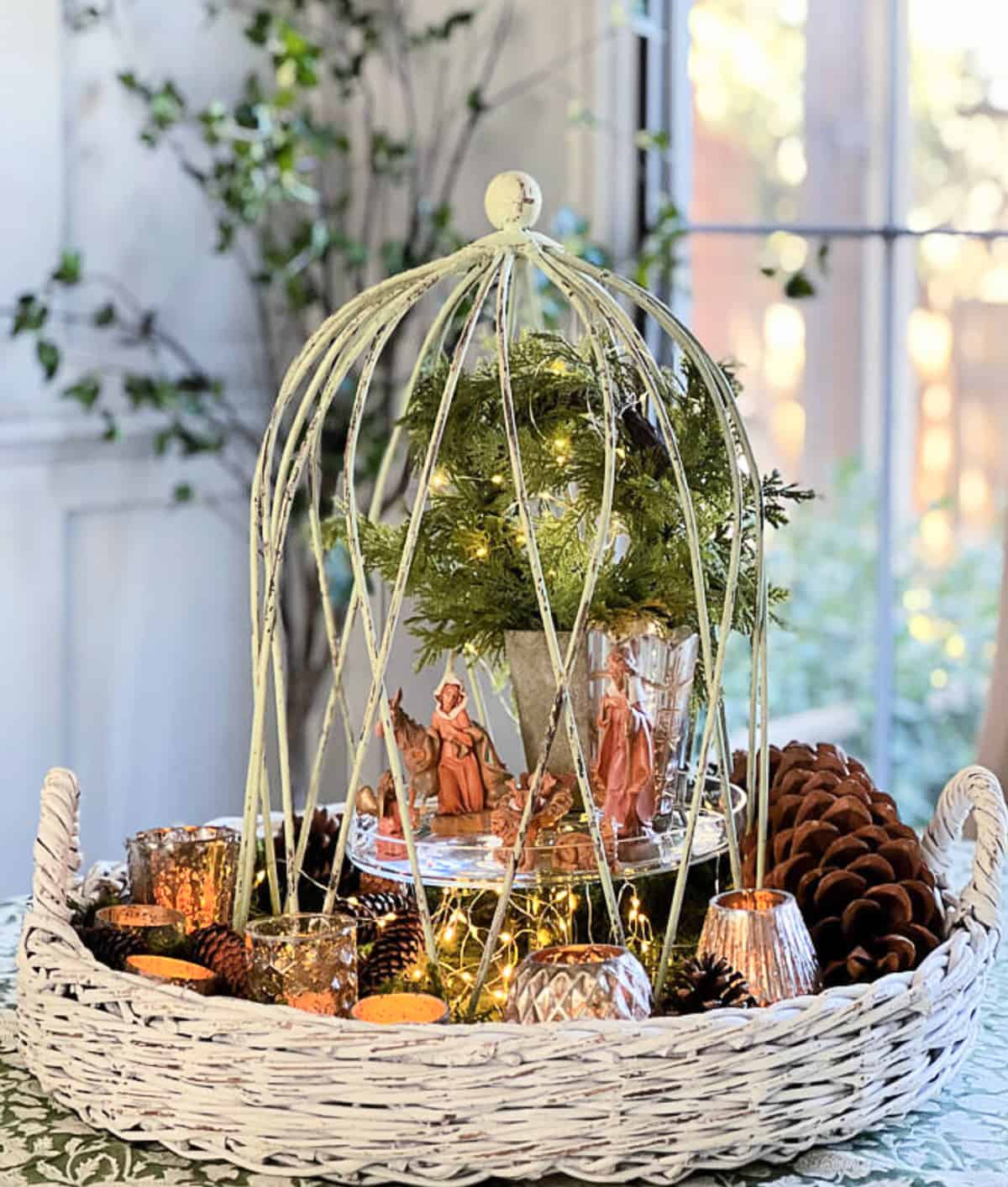 natitivy scene displayed under a wire cloche on a cake stand in the middle of a round tray with greenery