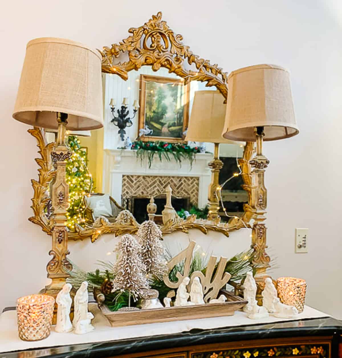 sideboard with lamps and a neutral nativity scene display with a gilted gold mirror hanging above