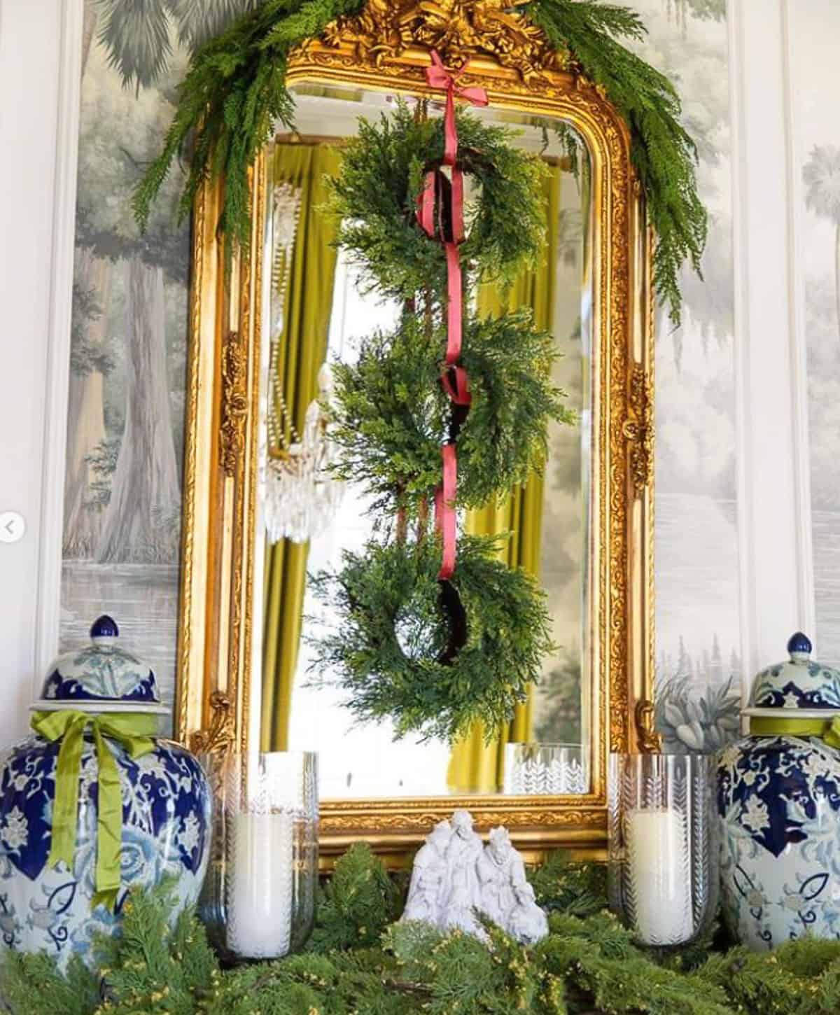nativity scene display on a sideboard surrounded by faux greenery with a gold mirror and wreaths hanging above.