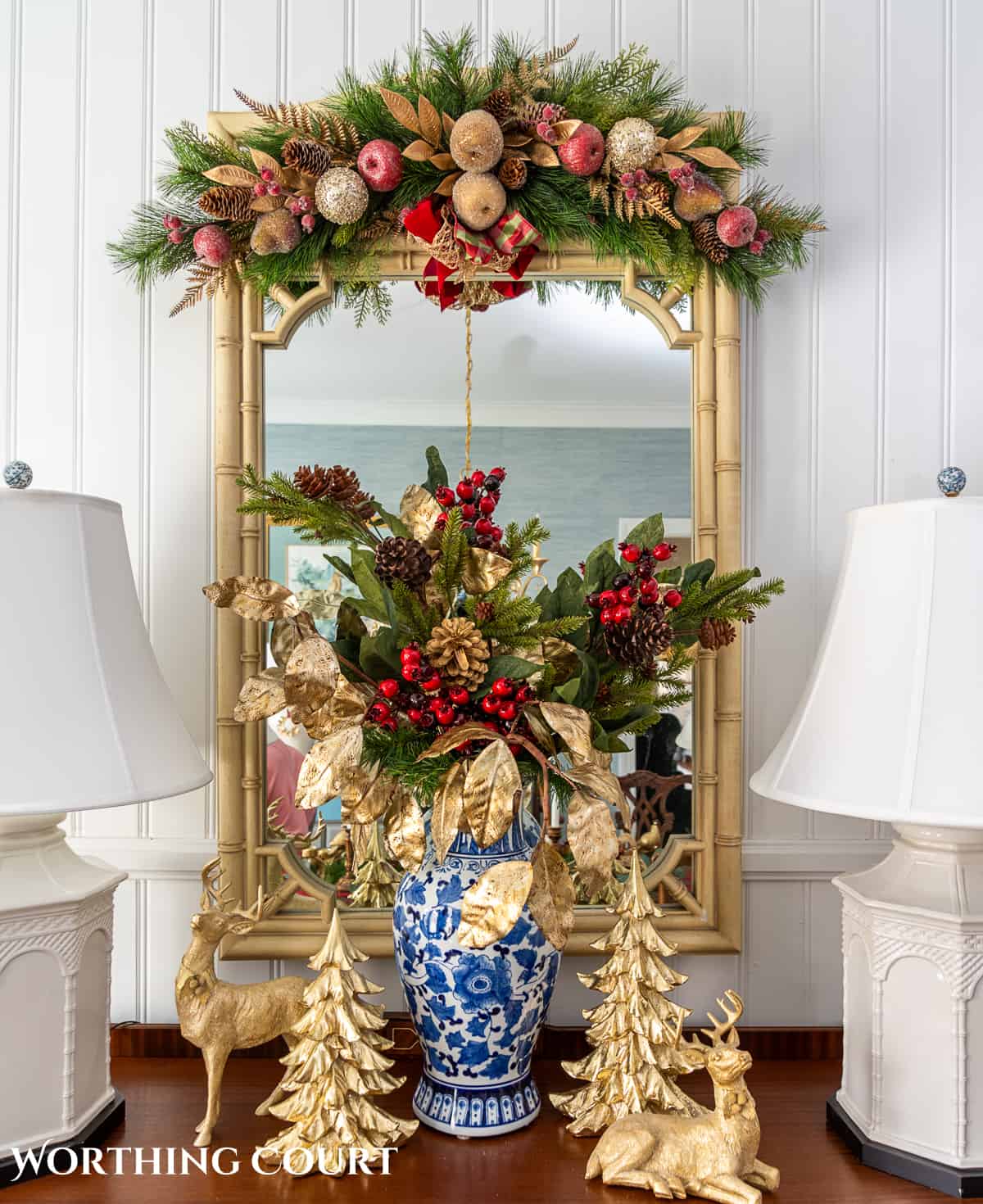 Christmas vignette on a sideboard with burgundy and gold stems in a blue and white vase flanked by gold deer and gold Christmas trees