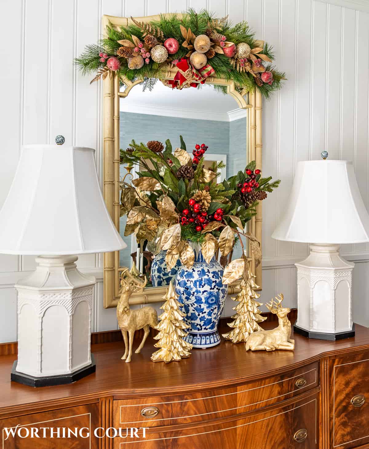 Christmas vignette on a sideboard with burgundy and gold stems in a blue and white vase flanked by gold deer and gold Christmas trees