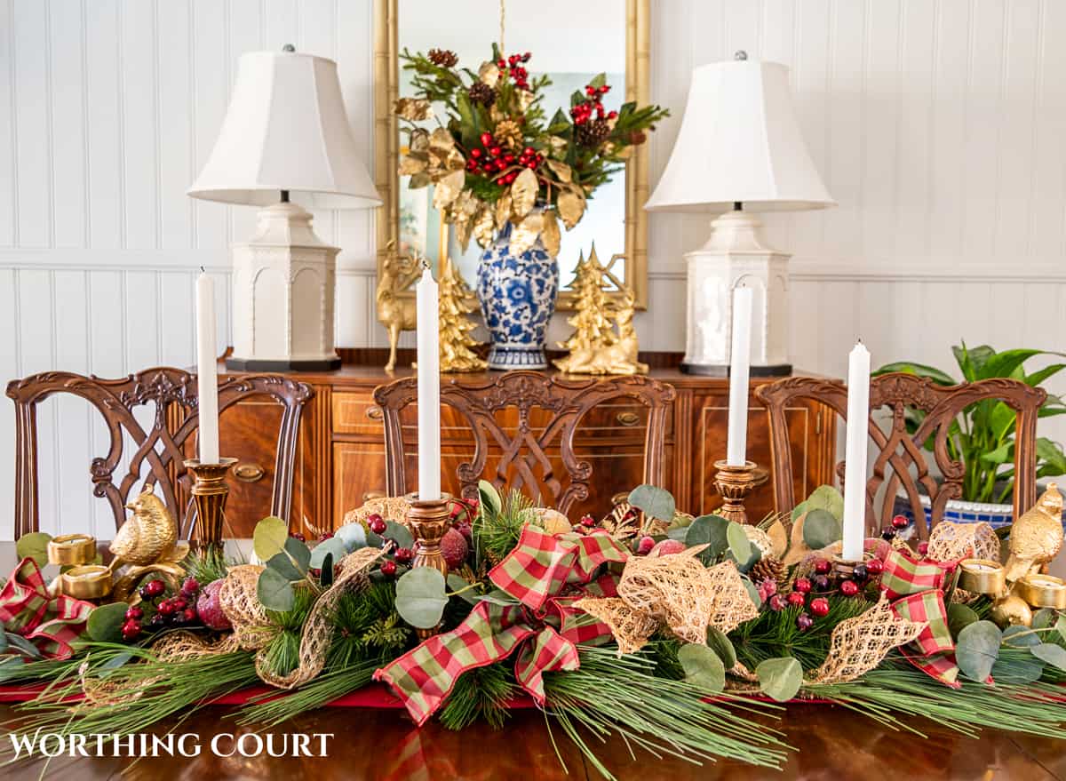 Christmas centerpiece on a wood dining room table made with burgundy, green and gold elements.