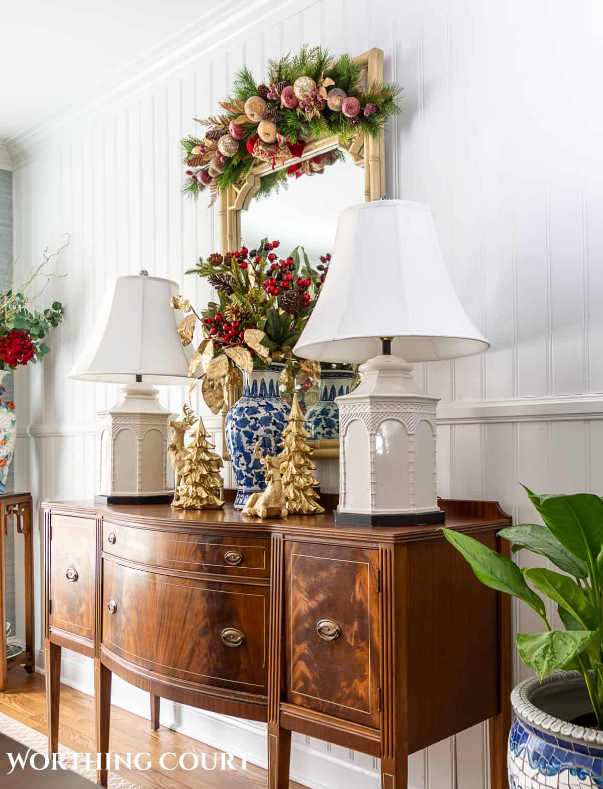 brown wood sideboard in front on white paneled wall with white lamps and Christmas decorations