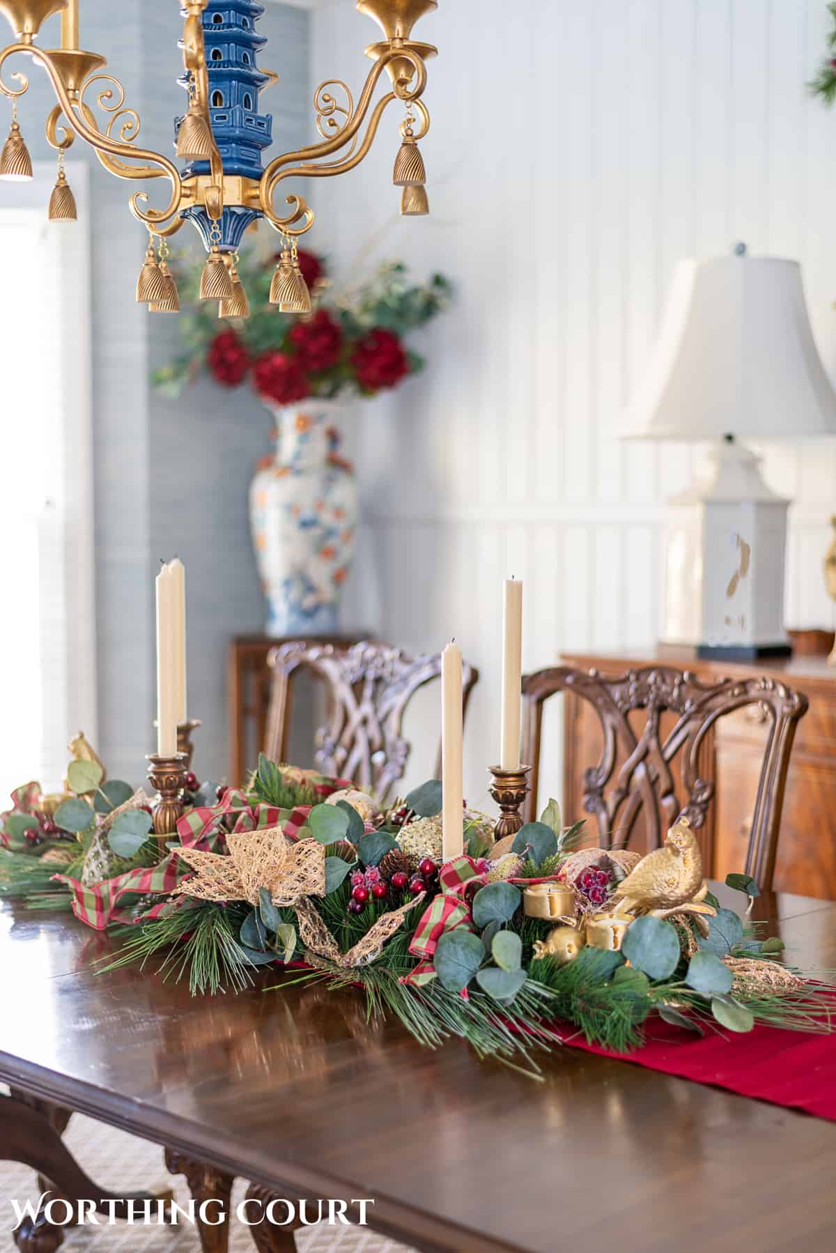 Christmas centerpiece on a wood dining room table made with burgundy, green and gold elements.