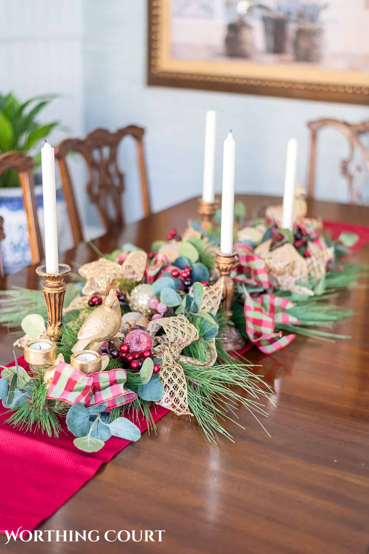 Christmas centerpiece on a wood dining room table made with burgundy, green and gold elements.