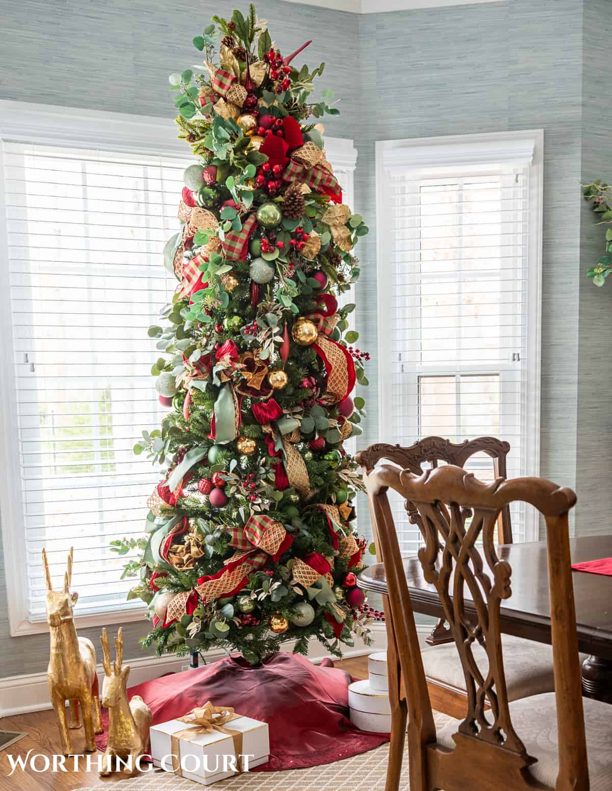 Slim Christmas tree with burgundy, green and gold decorations in a bay window.