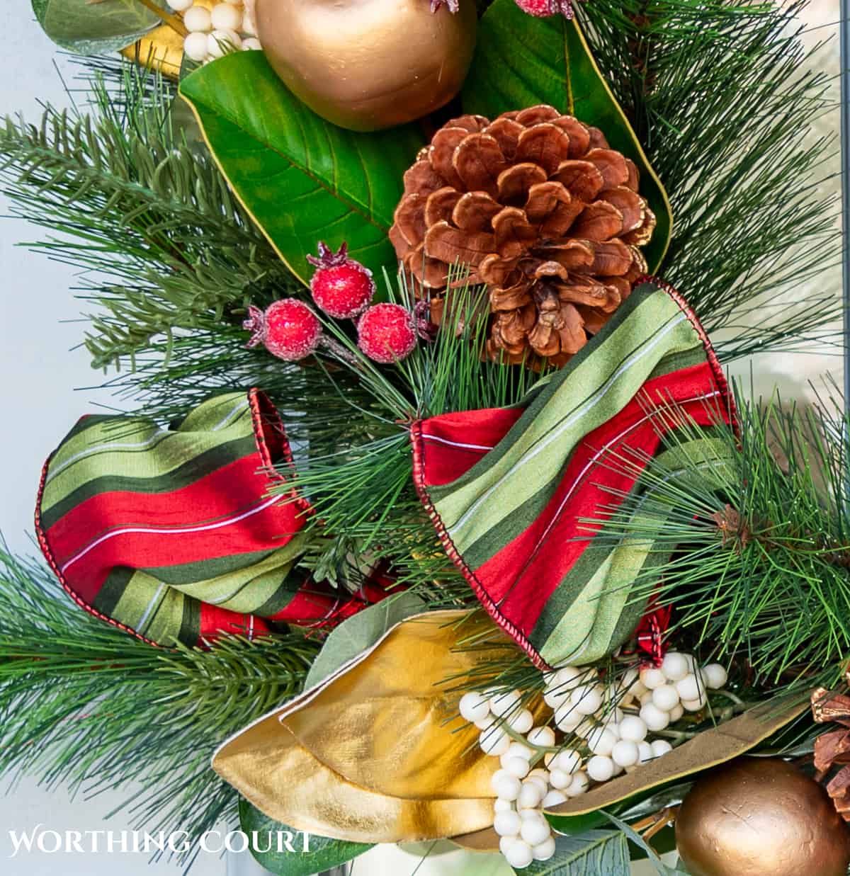 green and red striped silk ribbon on a pine wreath with gold fruit and leaves