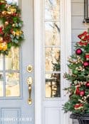 front door with a Christmas wreath and small tree with green and red ornaments in an urn beside it