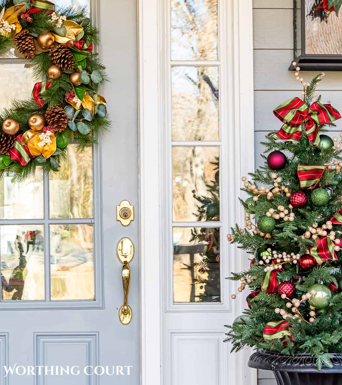 front door with a Christmas wreath and small tree with green and red ornaments in an urn beside it