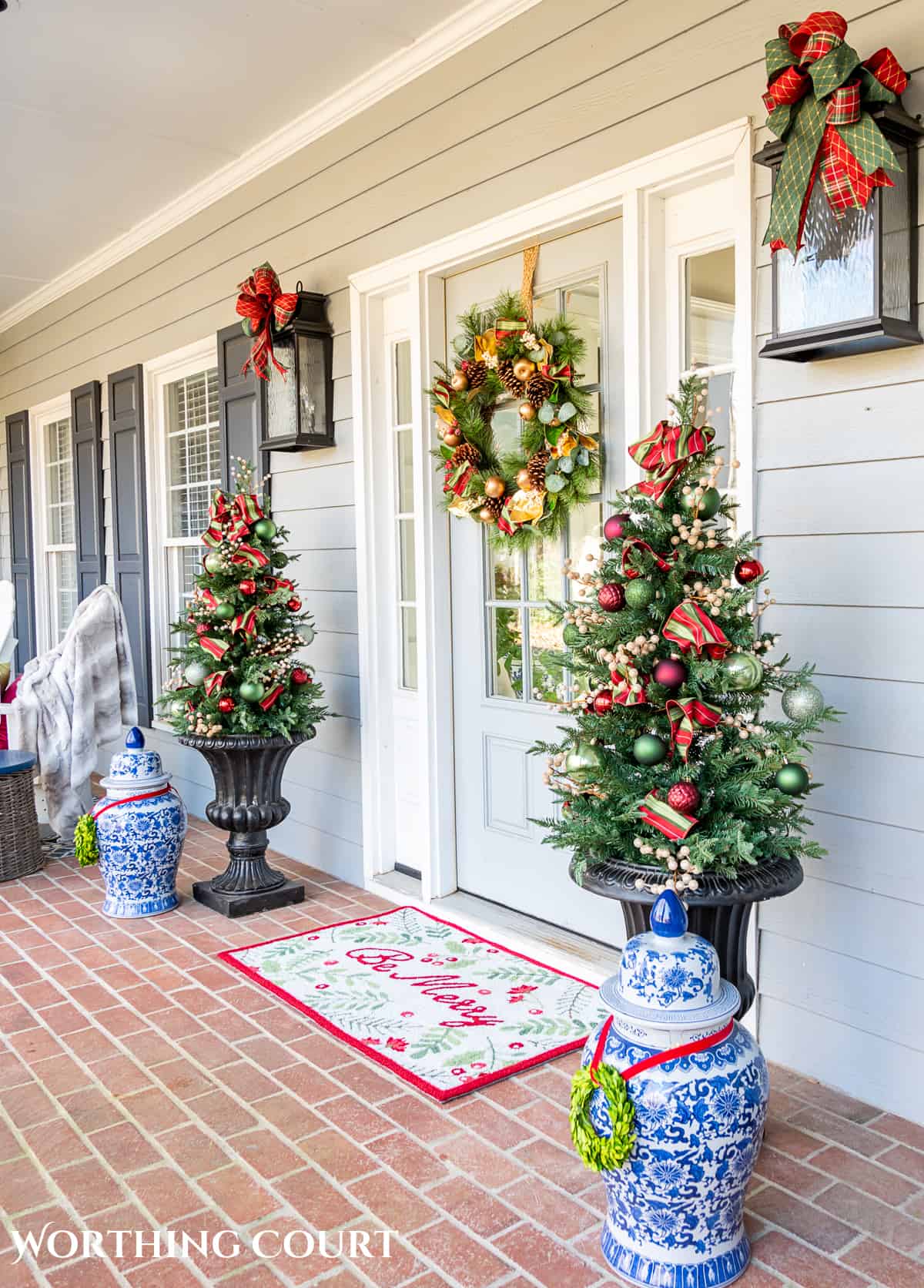 front door with a Christmas wreath flanked by urns with small trees with red, green and gold Christmas decorations on them