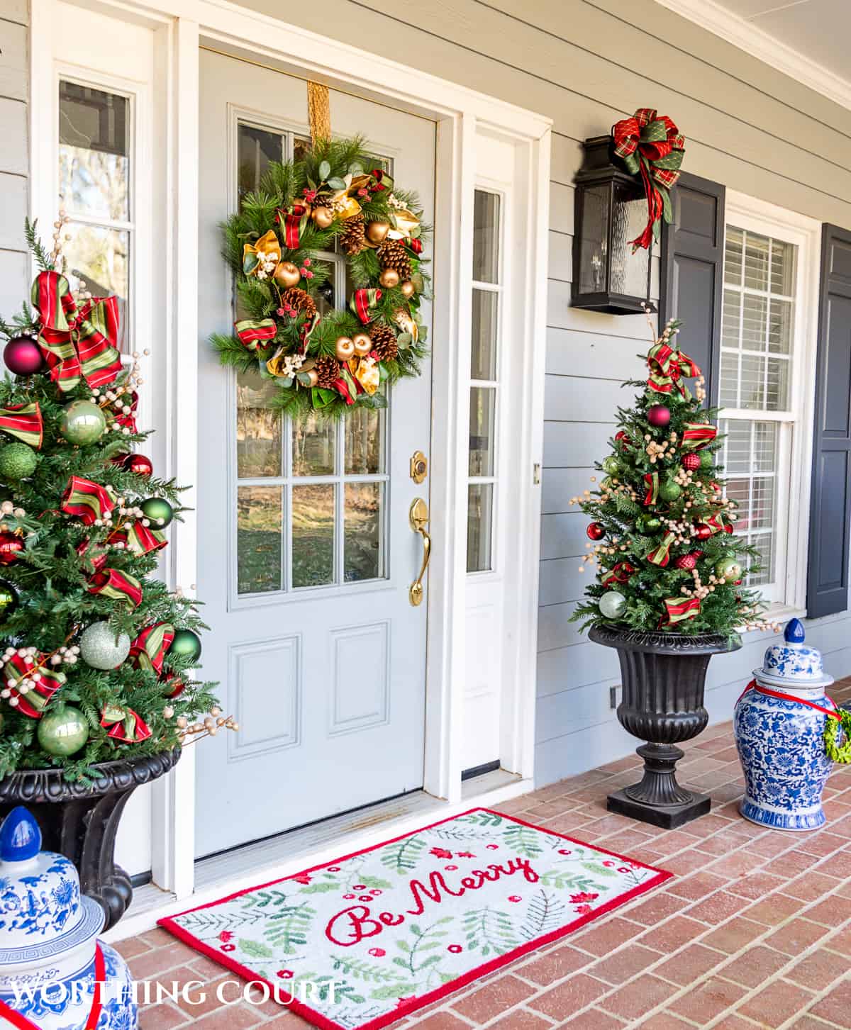 front door with a Christmas wreath flanked by urns with small trees with red, green and gold Christmas decorations on them