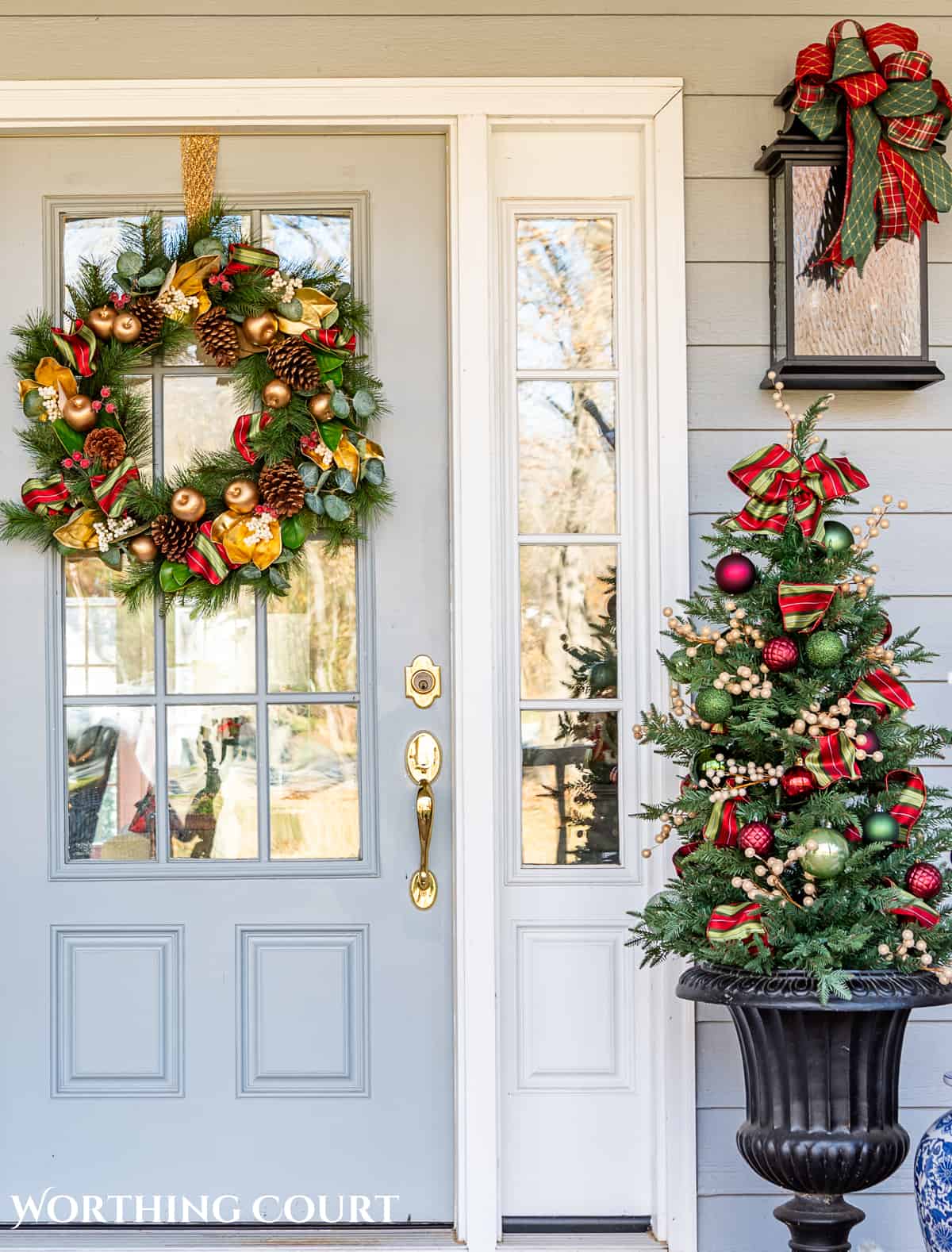 front door with a Christmas wreath and small tree with green and red ornaments in an urn beside it