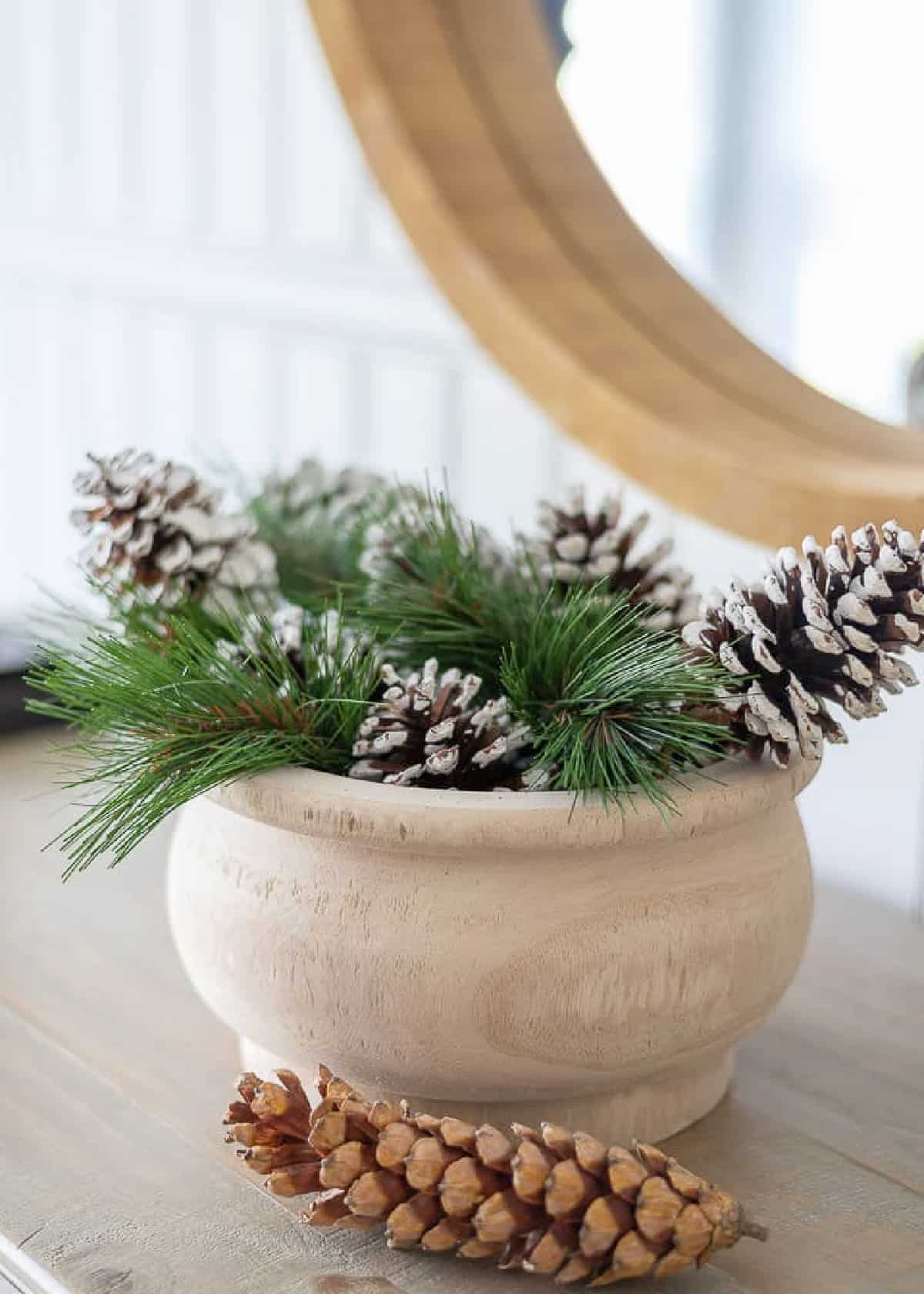 wooden bowl filled with faux evergreens and pinecones for winter decor