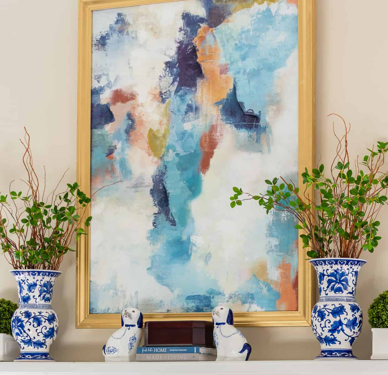 mantel with abstract art above and blue and white vases filled with stems on each end for winter decor