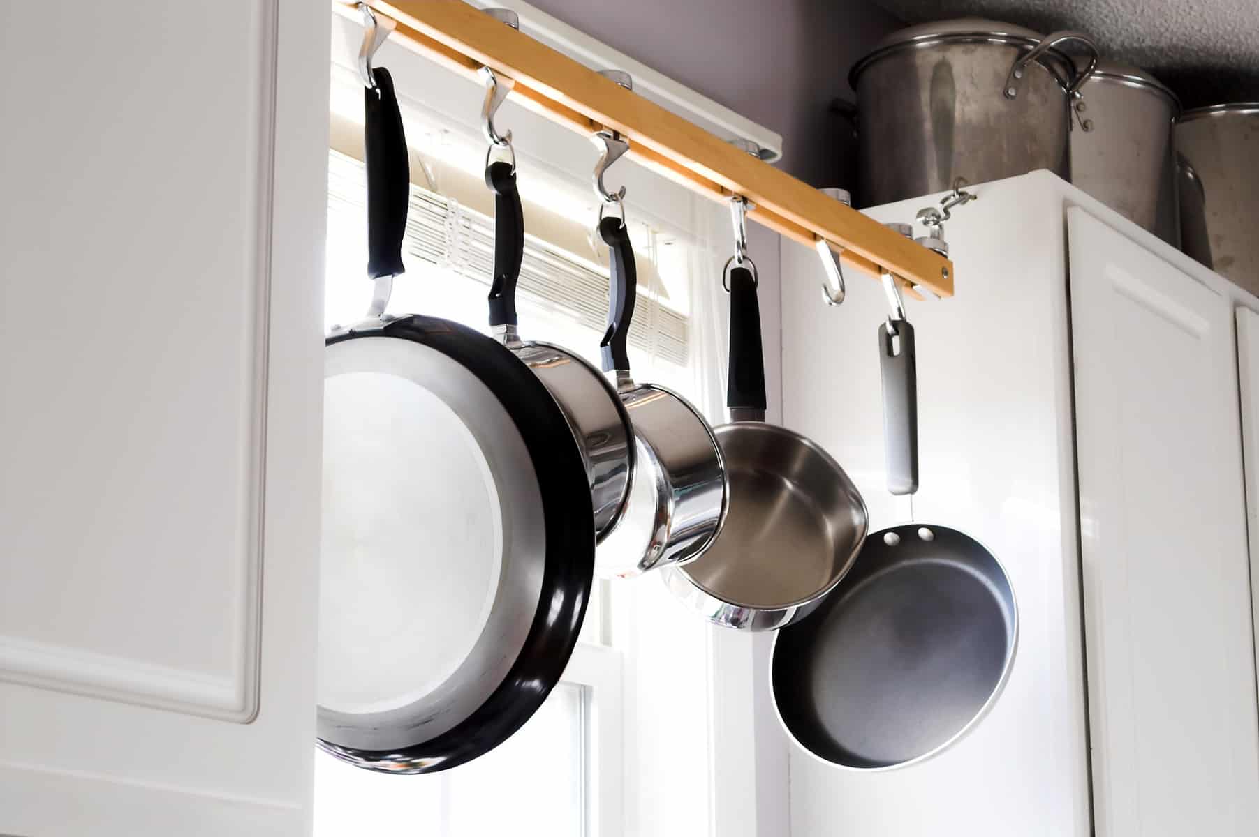 stainless steel cooking pans hanging in a window from hooks on a wooden rod