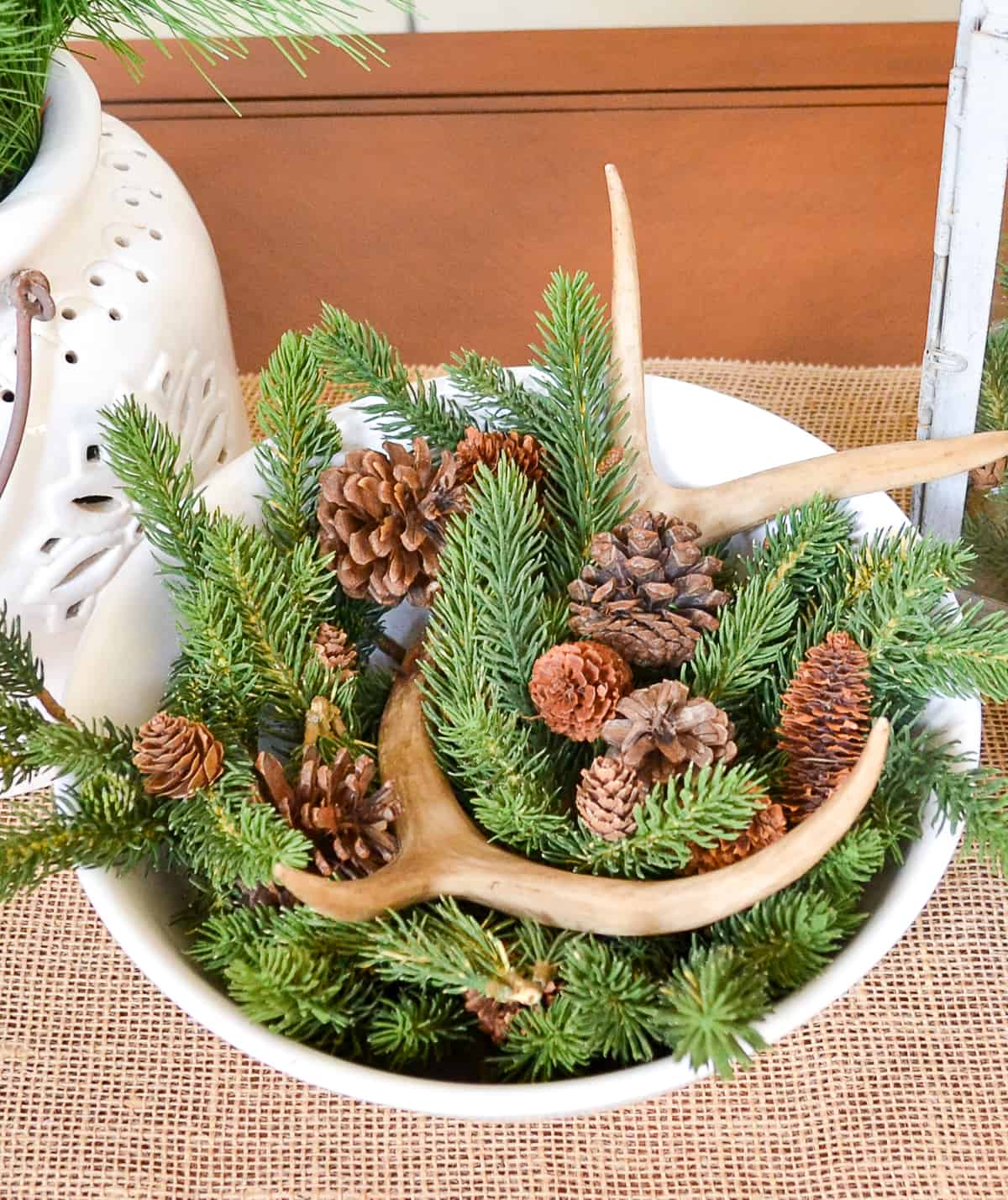 white bowl filled with faux greens, pinecones and faux antlers for winter decor