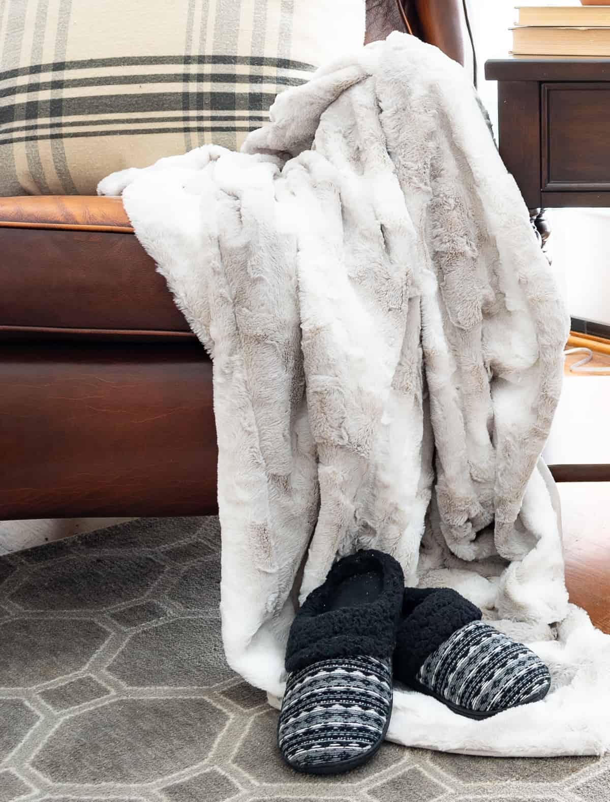faux fur blanket thrown over the arm of a brown leather chair and a pair of slipper