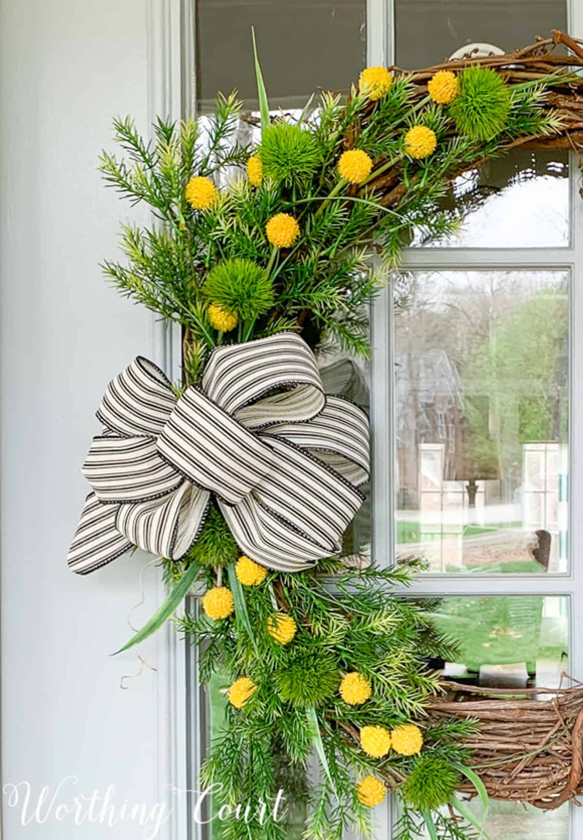 grapevine wreath decorated with yellow flowers, greenery stems, and burlap and black and white ribbon for spring