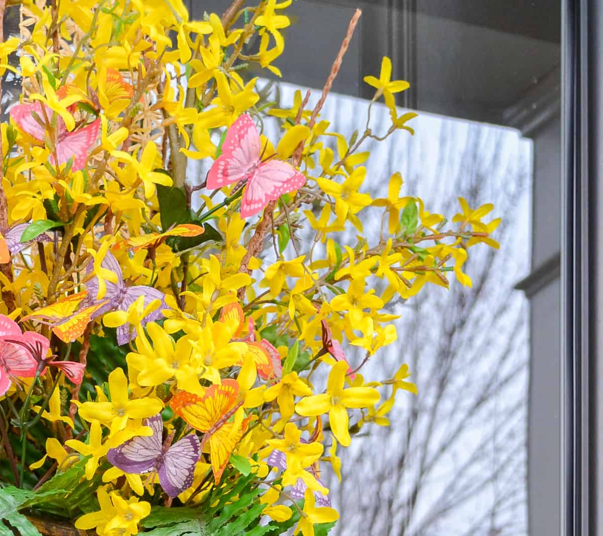 long hanging basket on a glass door filled with faux forsythia stems for spring