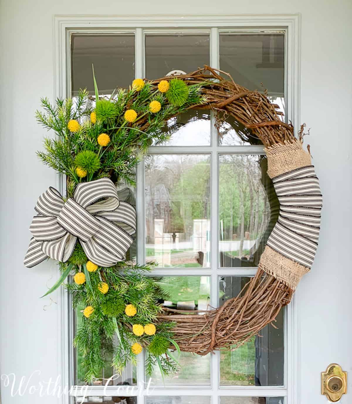 grapevine wreath decorated with yellow flowers, greenery stems, and burlap and black and white ribbon for spring