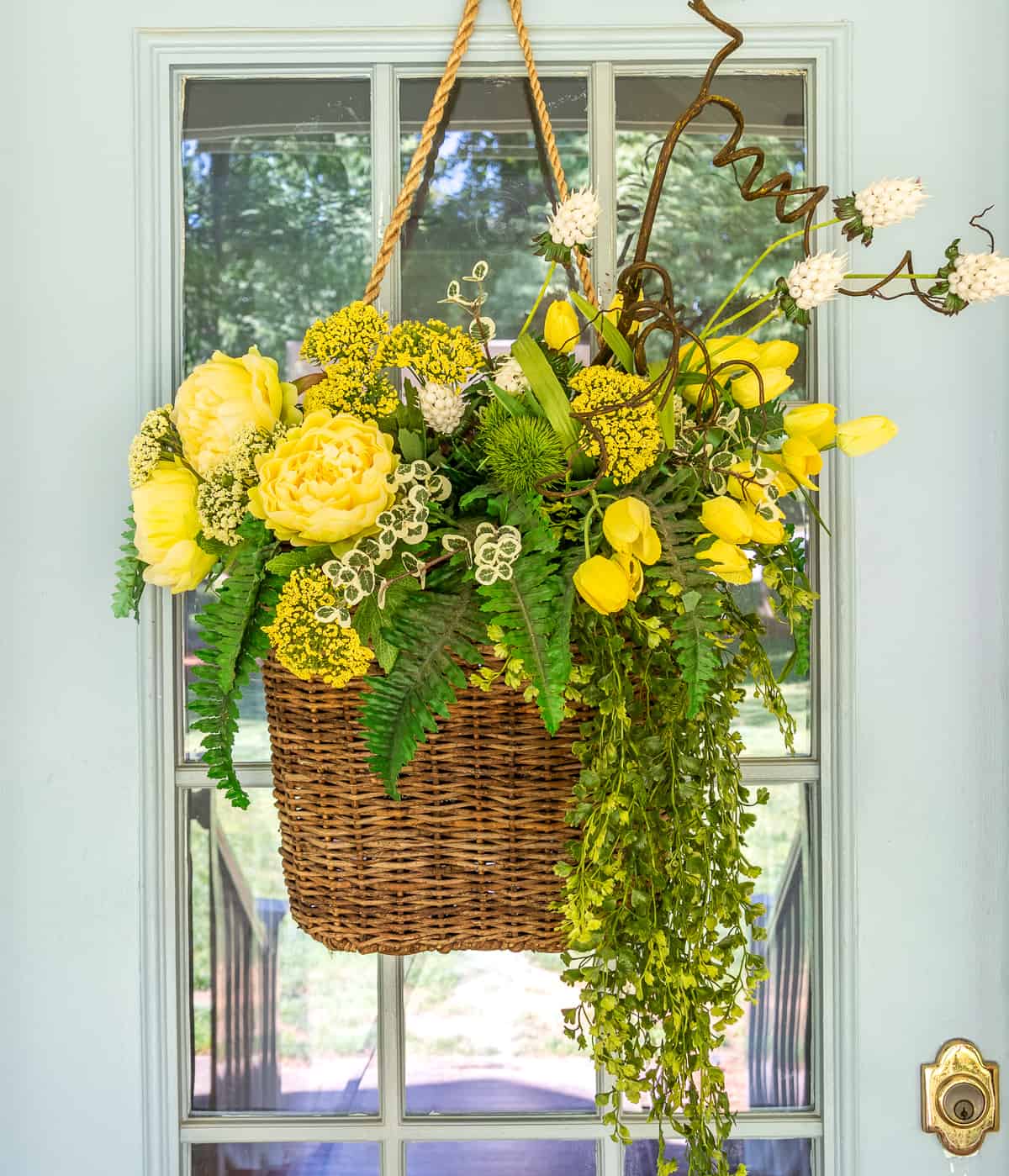 yellow flowers and greenery in a hanging basket on a gray front door for a spring door decoration
