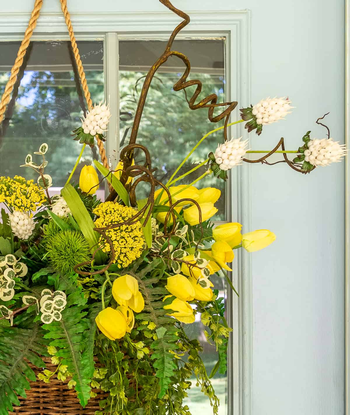 yellow flowers and greenery in a hanging basket on a gray front door for a spring door decoration