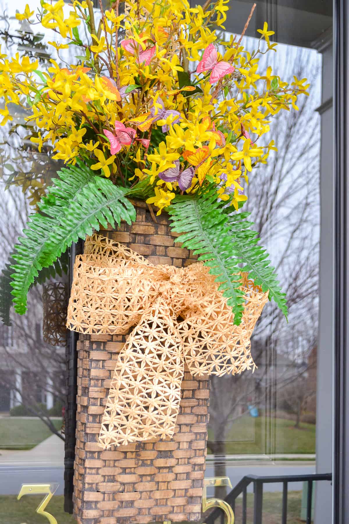 long hanging basket on a glass door filled with faux forsythia stems for spring