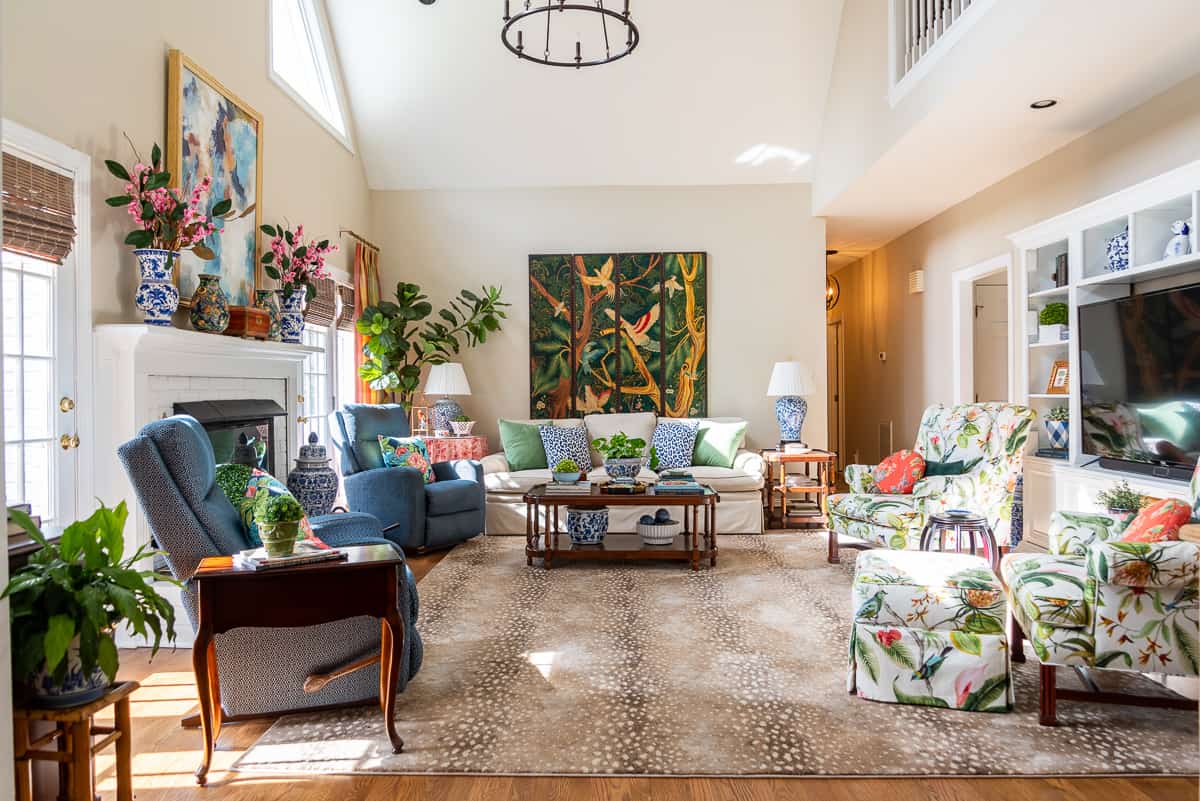 beige couch against the wall with a blue recliner beside it and colorful pillows on the couch and accessories on the tables