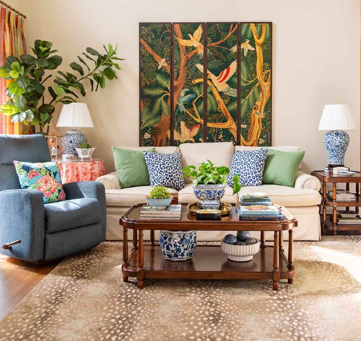 beige couch against the wall with a blue recliner beside it and colorful pillows on the couch and accessories on the tables