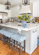 kitchen with white cabinets and a white tile backsplash and white quartz counters decorated with blue and white accessories and oranges stems in a vase