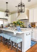 kitchen with white cabinets and a white tile backsplash and white quartz counters decorated with blue and white accessories and oranges stems in a vase