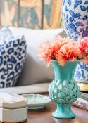 small turquoise vase of coral flowers on a wood end table beside a blue and white lamp
