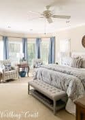 master bedroom with a large bay window decorated with neutral and blue bedding and furnishings