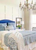 bed with blue and white linens and a blue upholstered headboard against a white board and batten wall