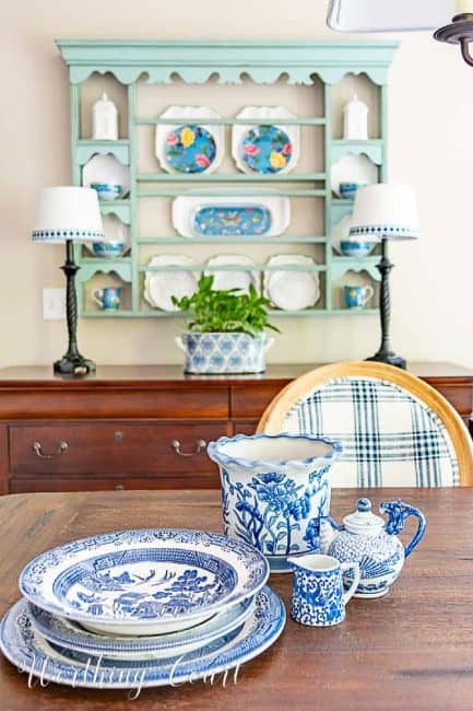 blue and white dinnerware stacked on a dining table in front of a blue plate rack