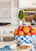 bowl of peaches in a blue and white checked bowl on a white kitchen counter
