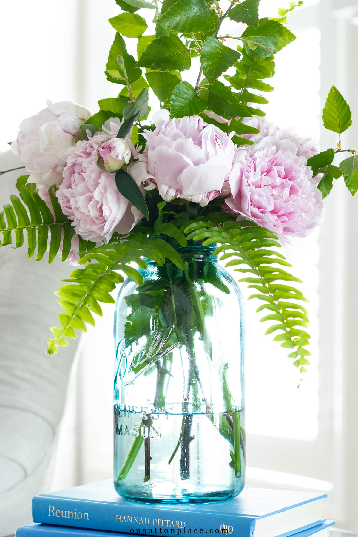 bouquet of pink peonies and fern leaves in an arrangement in a large blue mason jar