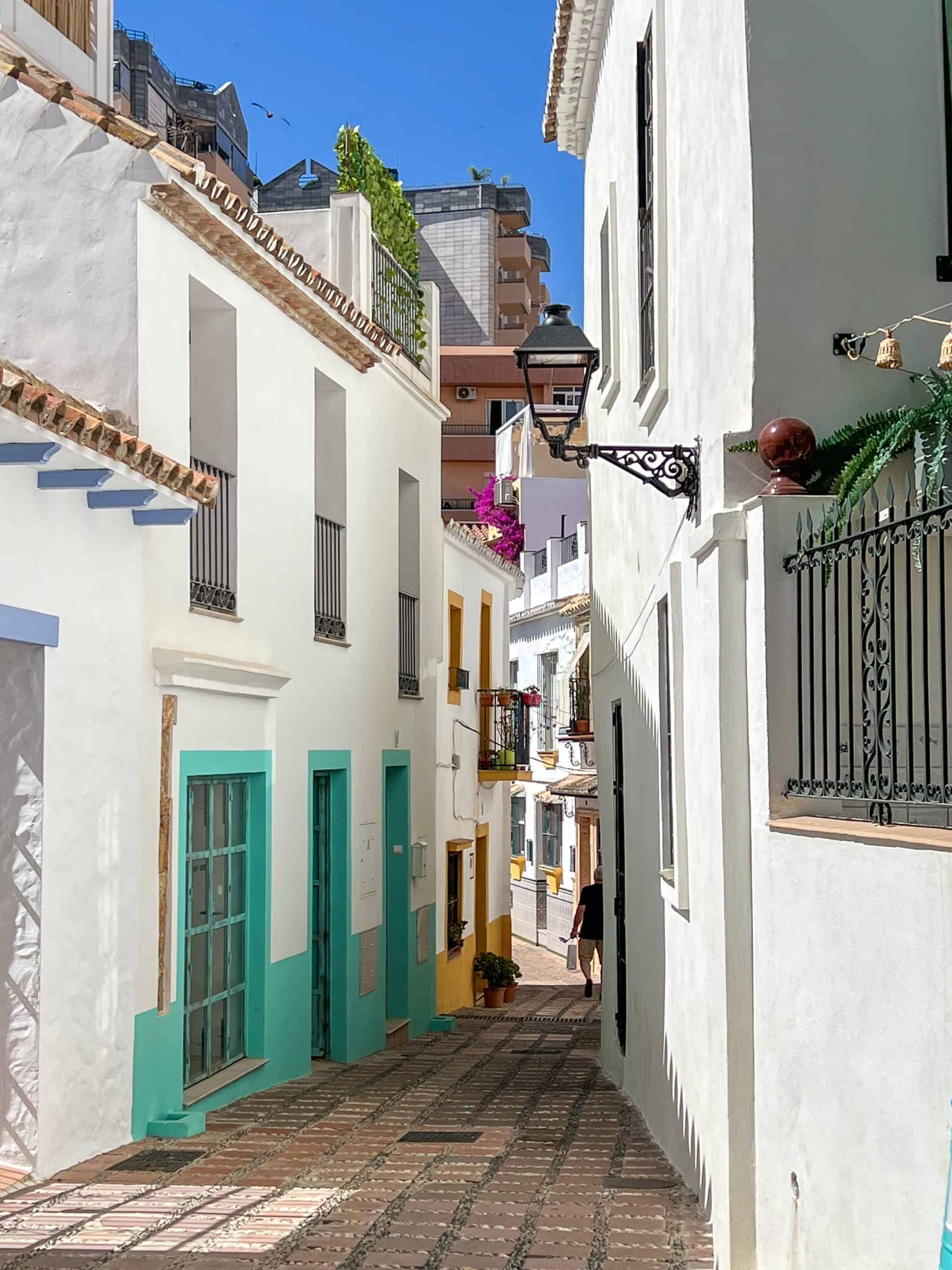 narrow alleyway between white stucco walls with turquoise doors