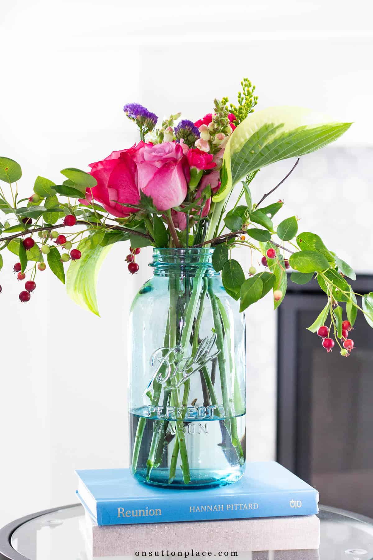 blue mason jar filled with a flower arrangement on top of a stack of books