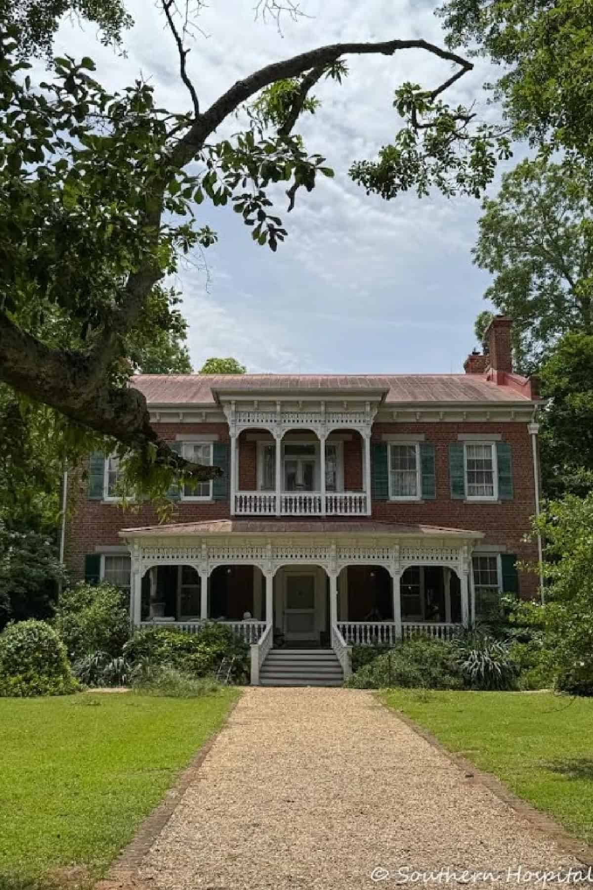 front of historic red brick home with white victorian style trim work and green shutters