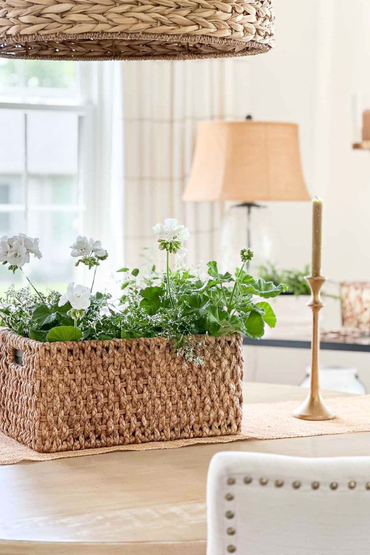 woven basket filled with white geraniums on a kitchen counter with candle and lamp in the background