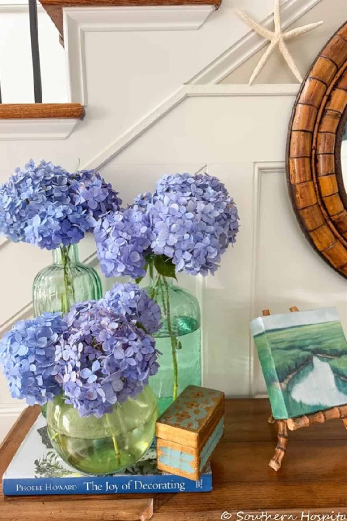 blue hydrangeas arranged in green glass bottles on a wooden chest