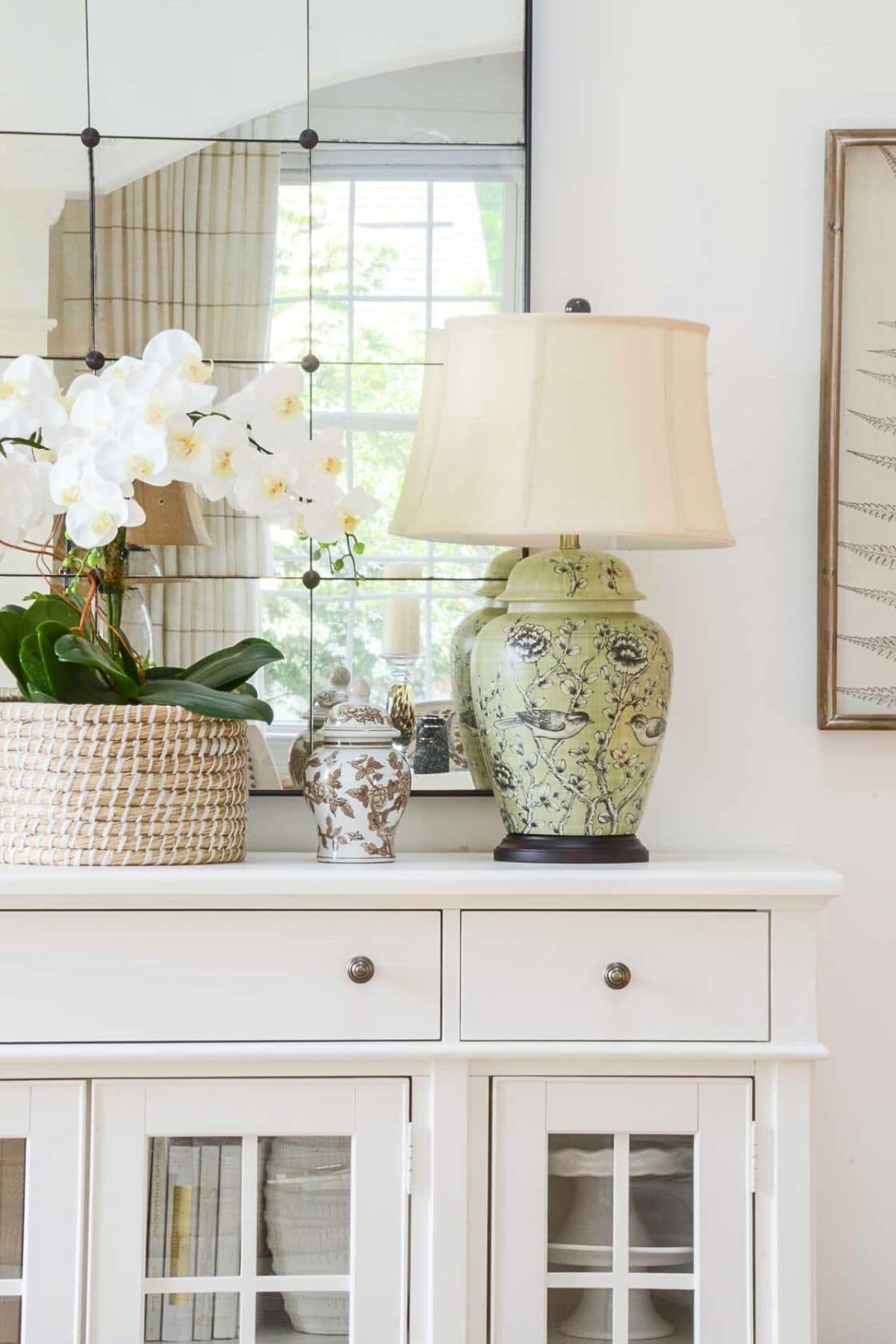 pale green lamp with a white shade on a white console table with a mirror above