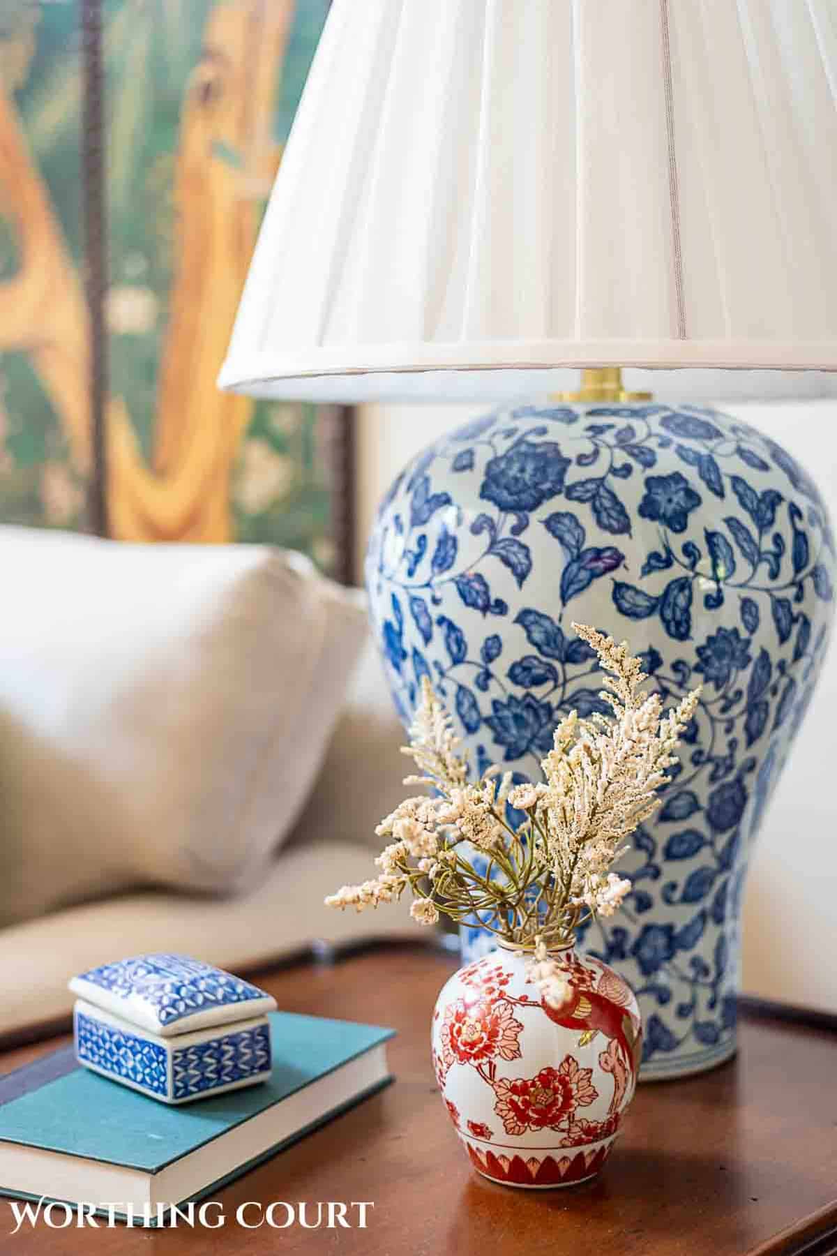 end table with blue and white chinoiserie style lamp and a rust and white chinoiserie vase filled with fall faux florals