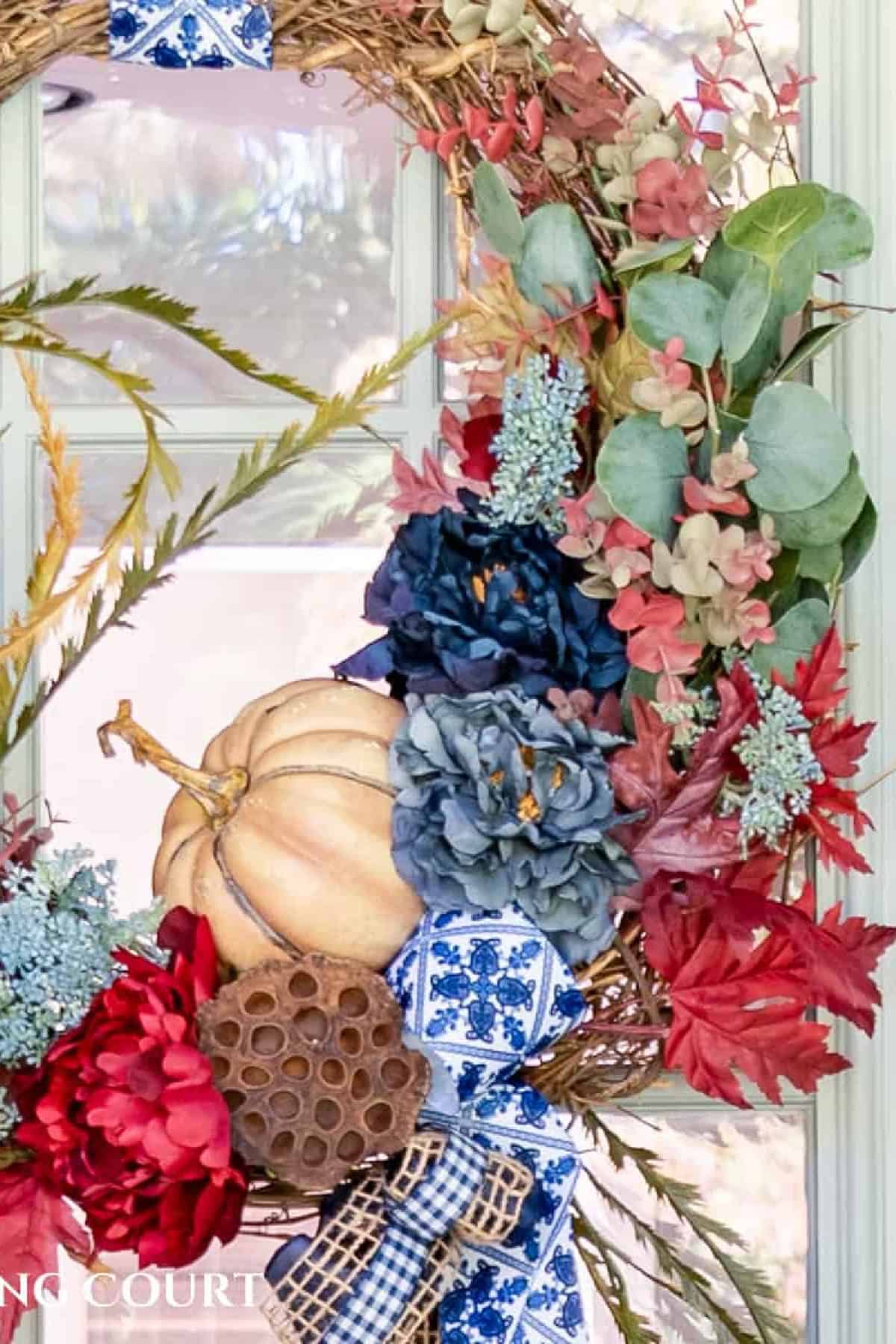 partial image of a fall wreath made with blue and burgundy flowers and pumpkin