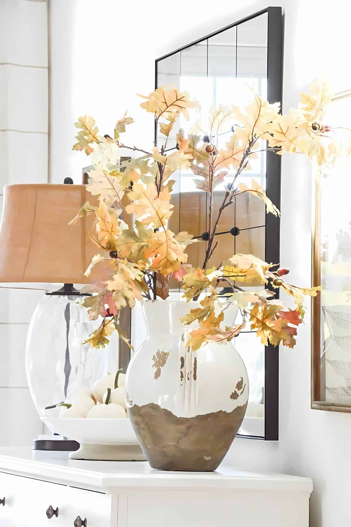 faux fall leaf stems in a white crockery vase on a white table