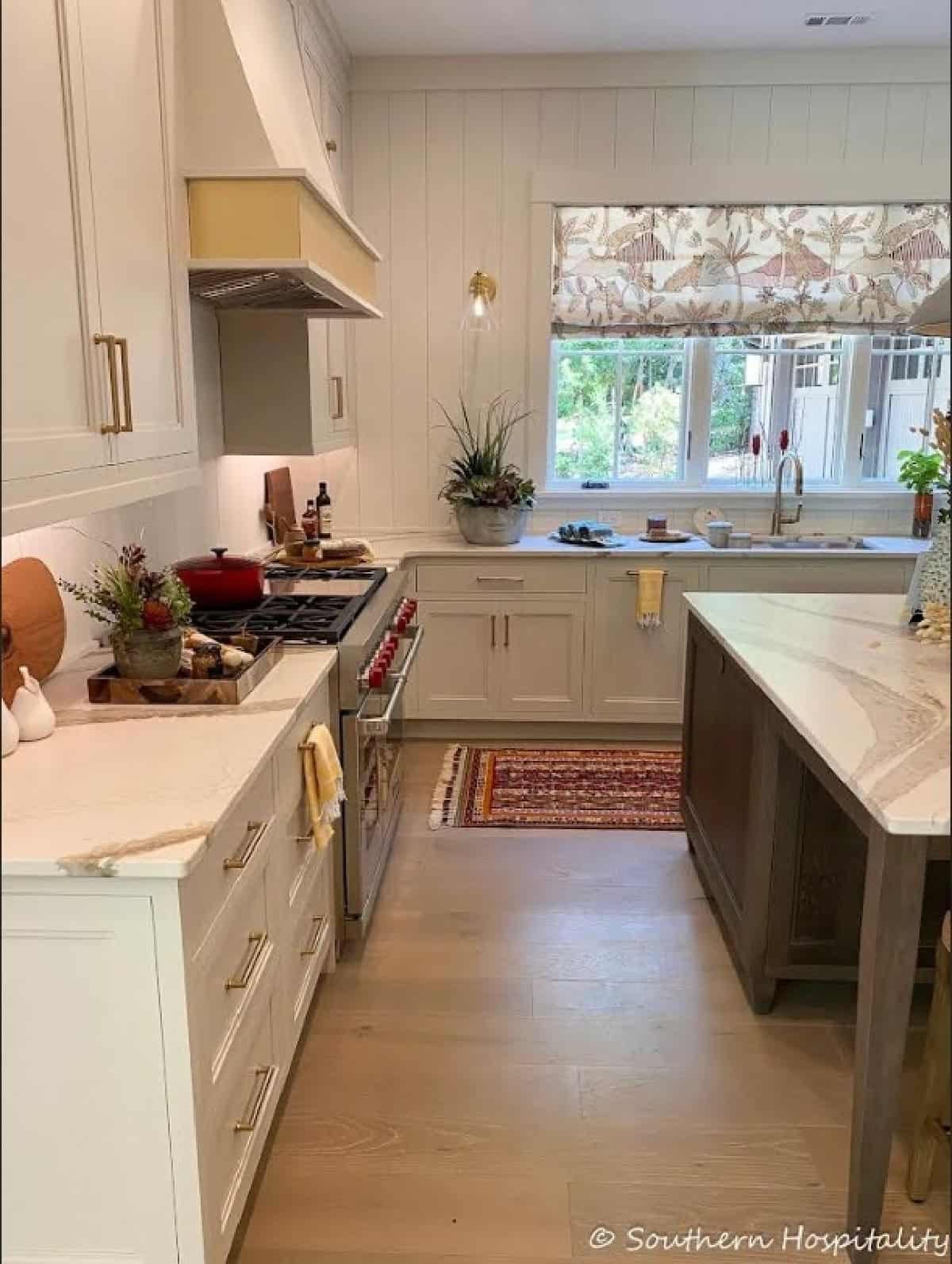 view into a kitchen between an island and counter with a gas range and large window above the sink