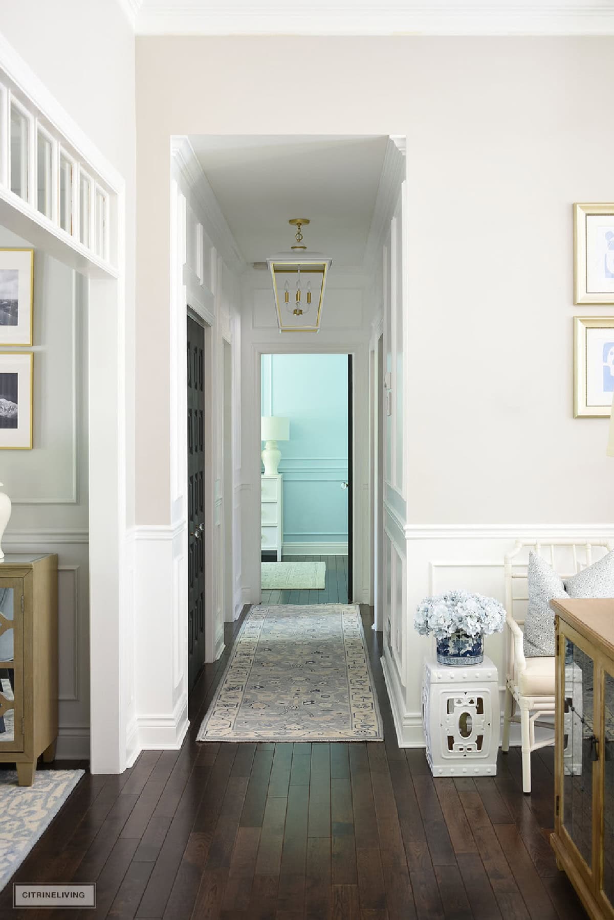 view down a hallway with white walls, millwork, dark wood floors, and a traditional style blue rug runner